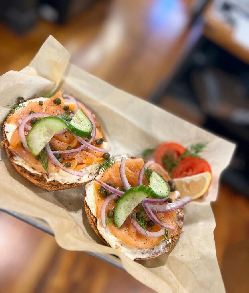 Indulge in the delightful flavors of a Lox bagel! This masterpiece combines a perfectly toasted bagel with delicate slices of salmon, creamy cream cheese, and a garnish of tangy red onions. To add a touch of freshness, a crisp cucumber is elegantly placed on top, turning this culinary creation into a true work of art.