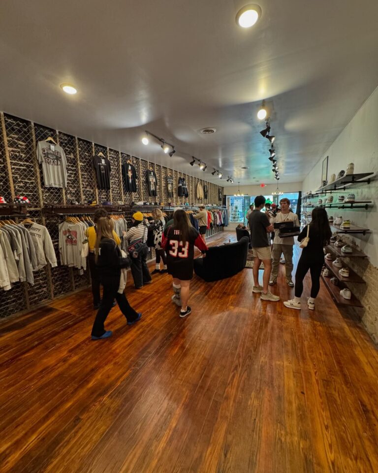 Interior of The Archive shop featuring wooden floors and clothing displays. Customers are browsing through racks of vintage apparel on the left wall and sneakers displayed on wooden shelves to the right. The shop's bright lighting and trendy atmosphere highlight its curated collection.