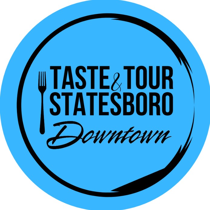 Logo for the Taste & Tour Statesboro Downtown event. The design features a blue circular background with a black fork icon and stylized black text reading 'Taste & Tour Statesboro Downtown.' A black brushstroke forms a partial ring around the edge of the circle.