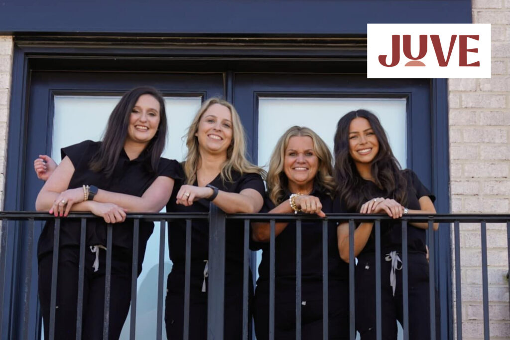 Four staff members from Juve Integrative Medicine & Wellness stand together on a balcony, smiling and leaning on a black railing in front of glass doors. The team members wear matching black uniforms, and the Juve logo appears in the top corner of the image, highlighting the clinic’s friendly and professional staff.