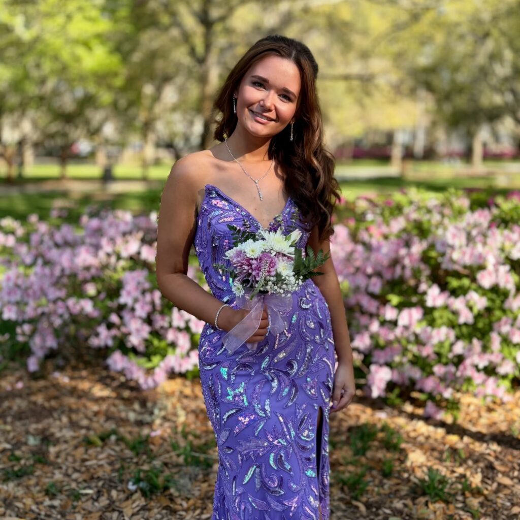 Student wearing a purple prom dress from Prom Bae posing with flowers on the Georgia Southern University campus in Statesboro, Georgia.
