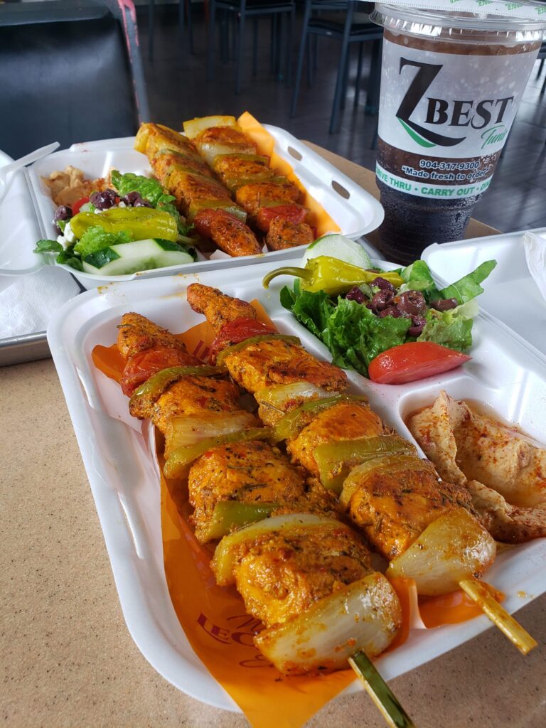 Grilled chicken and vegetable kabobs with salad, hummus, and drinks served in takeout containers at Z-Best in Statesboro.