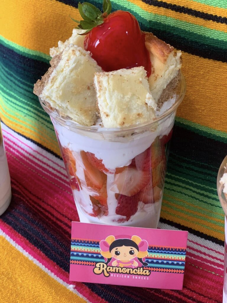Ramoncita Mexican Snacks dessert cup featuring strawberries, whipped cream, cheesecake pieces, and sweet strawberry topping.